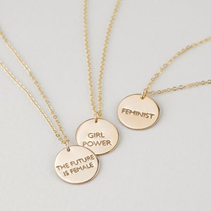 Puede incluir: Tres collares de oro con colgantes circulares. Los colgantes tienen el siguiente texto: "The future is female", "Girl Power" y "Feminist".