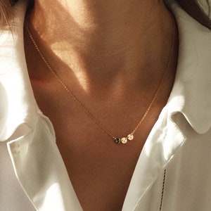 May include: A gold chain necklace with three small round pendants. The necklace is worn by a person with a white shirt.