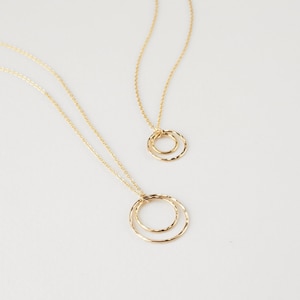 May include: Two gold necklaces with delicate chain links and textured circle pendants. The larger pendant is a double circle, while the smaller pendant is a single circle.