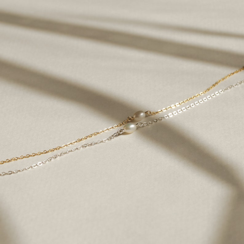 May include: Two delicate necklaces with small pearl accents. One necklace is silver and the other is gold.