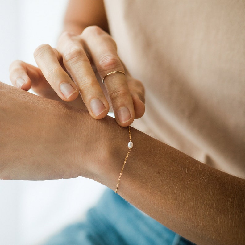 May include: A delicate gold chain bracelet with a single small pearl charm.