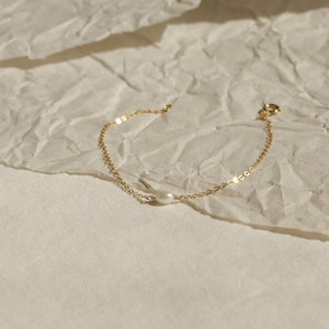 May include: A delicate gold chain bracelet with a single white pearl charm.