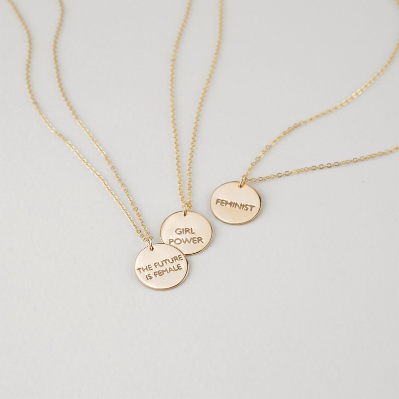 Puede incluir: Tres collares de oro con colgantes circulares. Los colgantes tienen el siguiente texto: "The future is female", "Girl Power" y "Feminist".