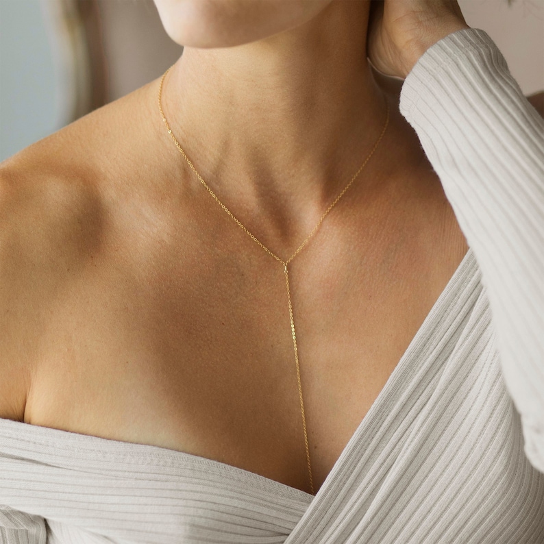 May include: A gold chain necklace with a long, thin pendant that hangs down the chest. The necklace is delicate and simple, and it would be a great addition to any jewelry collection.