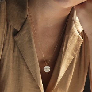 Puede incluir: Un collar de cadena dorada con un colgante redondo que dice "THE FUTURE IS FEMALE".