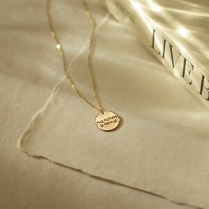 Puede incluir: Un collar de oro con un colgante redondo que dice "THE FUTURE IS FEMALE".