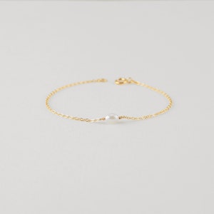 May include: A delicate gold chain bracelet with a single white pearl charm.