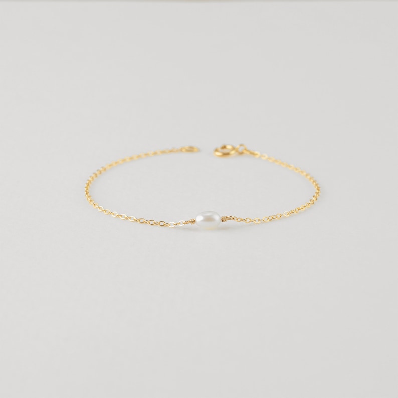 May include: A delicate gold chain bracelet with a single white pearl charm.
