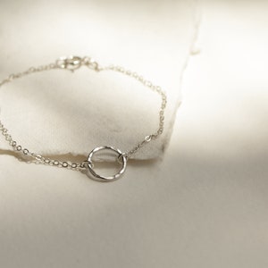May include: A delicate silver chain bracelet with a hammered circle pendant.