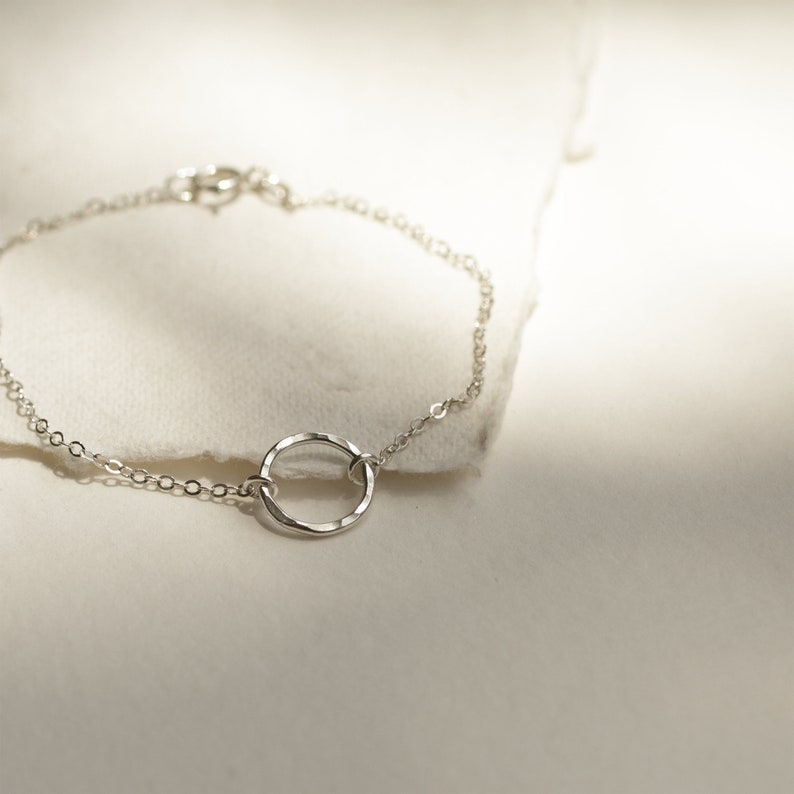 May include: A delicate silver chain bracelet with a hammered circle pendant.