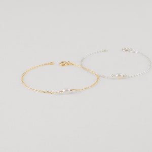 May include: Two delicate bracelets with a single pearl charm. One bracelet is gold and the other is silver.