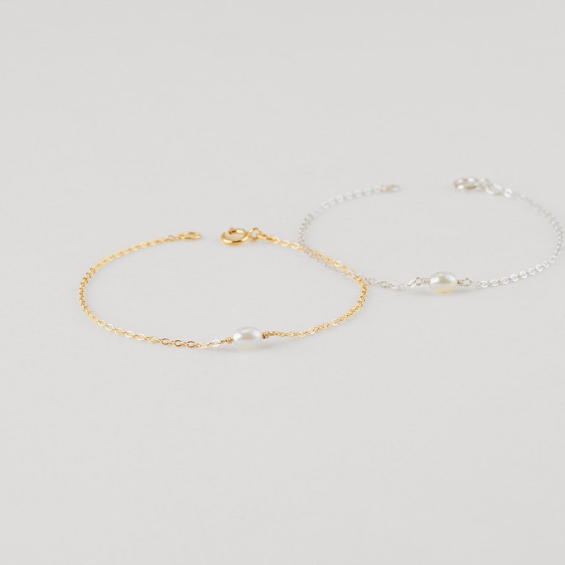 May include: Two delicate bracelets with a single pearl charm. One bracelet is gold and the other is silver.