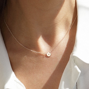 May include: A delicate gold chain necklace with a small round pendant featuring the letter "B".