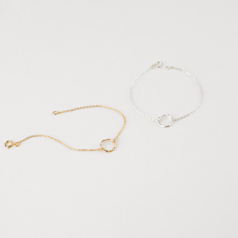 May include: Two delicate bracelets with a simple circle design. One bracelet is gold and the other is silver.