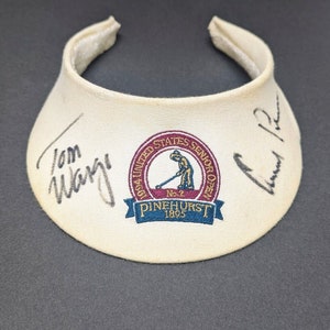 May include: White golf visor with a red, white, and blue embroidered logo that says "1994 United States Senior Open No. 2 Pinehurst 1895". The visor is signed by "Tom Weiskopf" and "Larry R"