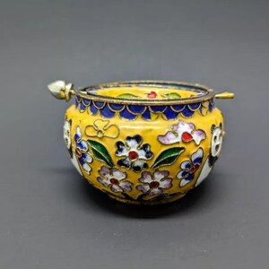 Pu&ograve; includere: Una piccola scatola portaoggetti in cloisonn&eacute; gialla con un motivo floreale e un coperchio con un piccolo pomo. La scatola &egrave; decorata con fiori bianchi, blu, verdi e rossi.
