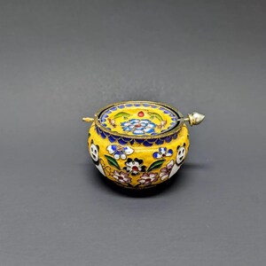Pu&ograve; includere: Una piccola scatola rotonda in smalto cloisonn&eacute; gialla con un motivo floreale e un coperchio in argento. Il coperchio ha un piccolo pomo in argento sulla parte superiore.