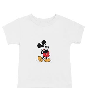 May include: White t-shirt featuring a classic cartoon image of Mickey Mouse. The iconic character is depicted in his signature red shorts, yellow shoes, and black gloves. The shirt is a short-sleeved crew neck.