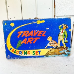 Puede incluir: Caja vintage de juego de colorear Travel Art con fondo azul y una estela de cometa amarilla. La caja presenta a un niño y una niña coloreando en un mapa del mundo. El texto en la caja dice "Travel Art Coloring Set" y "By Hasenfeld Bros. Inc.  Patented U.S.A. No. 2272".