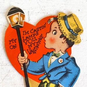 May include: A vintage Valentine's Day card featuring a cartoon boy in a blue suit and straw hat holding a lamppost. The card is shaped like a heart and has the text "I'm castin' lamps on you, my Valentine".
