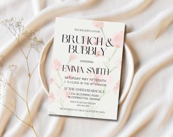 May include: A brunch invitation with the text "Brunch & Bubbly" honoring Emma Smith. The invitation is decorated with pink floral accents and is set on a white plate and a cream-colored fabric background.