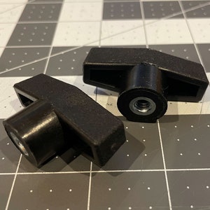 May include: Two black T-handle knobs with a threaded insert. The knobs have a textured surface and are designed for easy grip and tightening. They are likely used for adjusting or securing components in various applications.