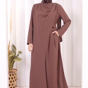 May include: A long-sleeved, floor-length brown dress featuring a wrap-style front panel, a high neckline, and side pockets. The garment is paired with a matching brown headscarf that has thin, light-colored vertical stripes throughout.