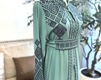 Puede incluir: Un vestido largo y fluido de color verde mar con intrincados patrones bordados en negro. El vestido presenta un cuello alto, mangas largas y un cinturón a juego. El bordado se concentra en el corpiño, las mangas y el cinturón.