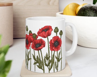 May include: White ceramic mug with a red poppy flower design. The mug has a handle and is sitting on a beige coaster.