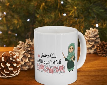 May include: White ceramic mug with a green and brown illustration of a woman wearing a headscarf and holding a book and pointer. The text on the mug reads "شكرا معلمتي لك كل الحب و التقدير" which translates to "Thank you teacher, all my love and appreciation".