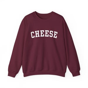 May include: Burgundy sweatshirt with the word "CHEESE" printed in white in a collegiate font.
