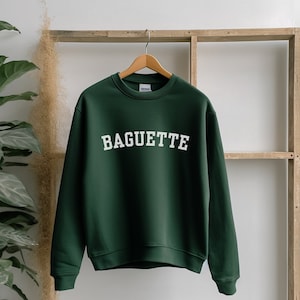 Może przedstawiać: Zielony sweter z nadrukiem "BAGUETTE" w kolorze białym na przodzie.