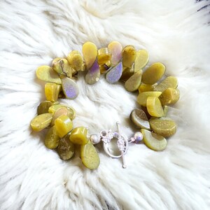 May include: A green and yellow gemstone bracelet with a silver toggle clasp. The bracelet is made of many small, teardrop-shaped stones.