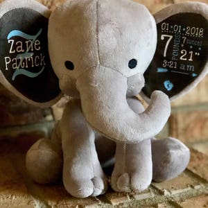 May include: Gray plush elephant with embroidered ears. One ear says "Zane Patrick" in blue and black lettering. The other ear says "01.01.2018 7 pounds 7 ounces 21" 3:21 am" in black and white lettering.