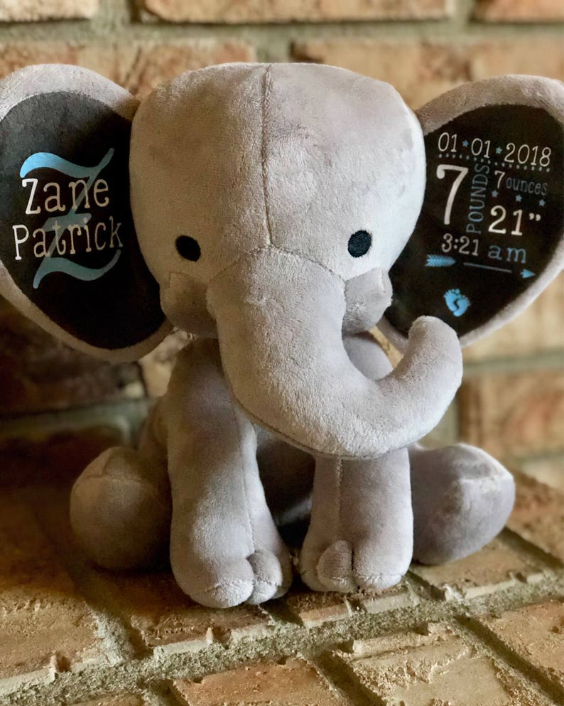 May include: Gray plush elephant with embroidered ears. One ear says "Zane Patrick" in blue and black lettering. The other ear says "01.01.2018 7 pounds 7 ounces 21" 3:21 am" in black and white lettering.