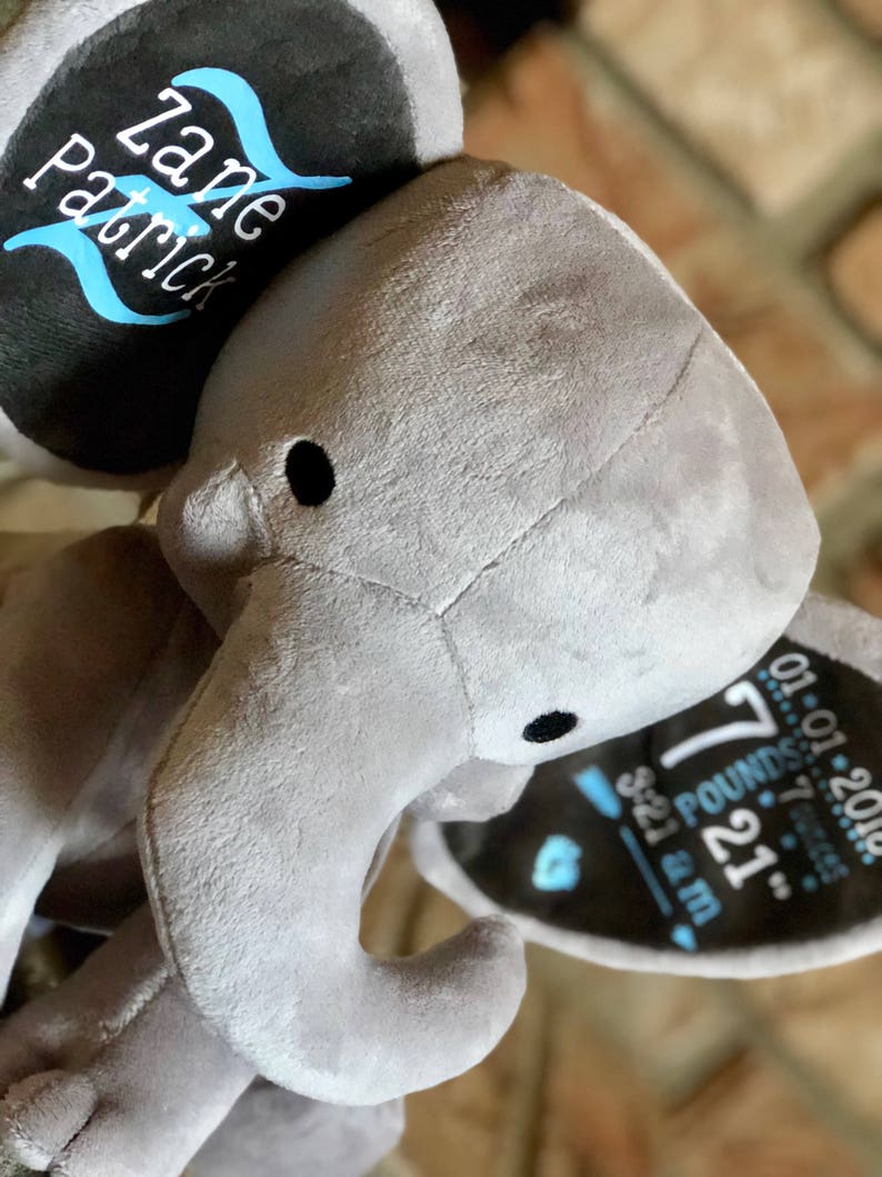 May include: Gray plush elephant stuffed animal with a black and blue embroidered tag on its ear. The tag reads "Zane Patrick" and includes the baby's birth information: "7 lbs 21 oz, 5:21 a.m., 01.01.2018".