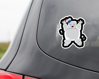 May include: A gray cartoon character sticker with a black outline is affixed to a car window. The character has a red and white hat and is waving its arms. The sticker is a fun and whimsical design.