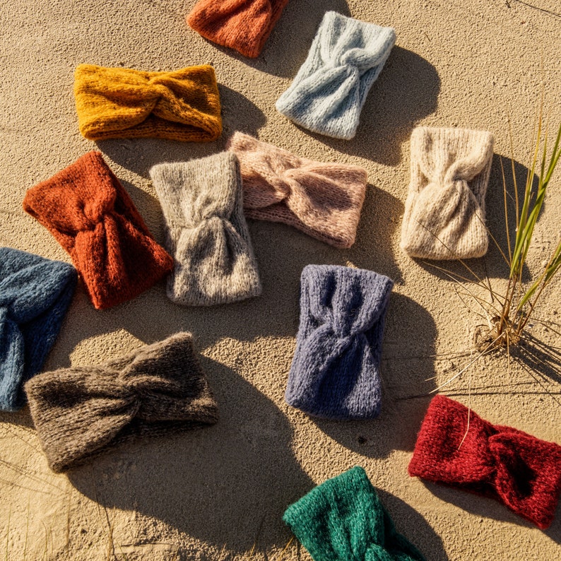 Puede incluir: Surtido de diademas de punto de colores, en varios colores, incluyendo azul, verde, rojo, marr&oacute;n y beige. Las diademas est&aacute;n dispuestas sobre una superficie arenosa.