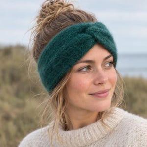 Op de afbeelding: Een donker bosgroene gebreide hoofdband met een centraal gedraaid knoopdetail. Het accessoire is gemaakt van een zacht, getextureerd garenmateriaal en is ontworpen om rond het hoofd te worden gedragen om de oren te bedekken met een brede band.