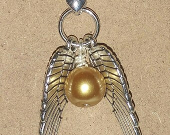 May include: Silver-toned necklace featuring a golden sphere pendant with silver wings. The pendant is suspended from a delicate chain. The jewelry is set against a neutral background. The text "Jewelry by Mindy" is visible.