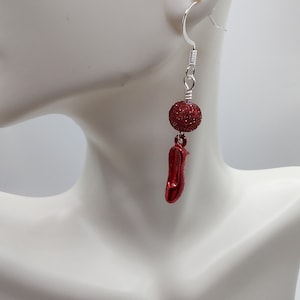 Könnte beinhalten: Einzelner Ohrring mit silbernem Haken, rotem Glitzerball und rotem, abstrakt geformtem Anhänger. Der Ohrring wird auf einer weißen Schaufensterpuppe präsentiert. Der Text "Jewelry By Mindy" befindet sich in der unteren rechten Ecke.