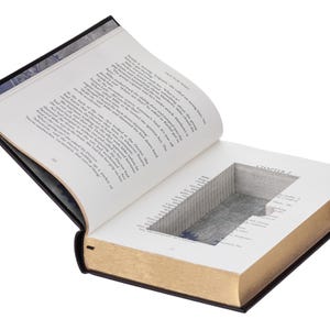 May include: A hardcover book with a rectangular hollow compartment carved into the center of its pages. The book is open to Chapter 2, revealing white paper pages with black printed text and gold-toned edges on the outer side of the pages.