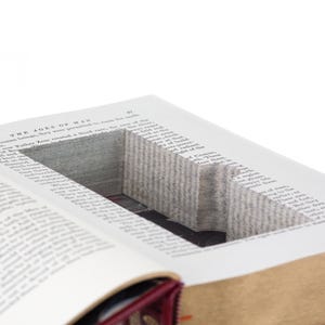 May include: A hardcover book with a rectangular hollow compartment carved into the center of its pages. The visible text at the top of the page reads The Ages of Man. The book features a deep red spine and gold-toned page edges.