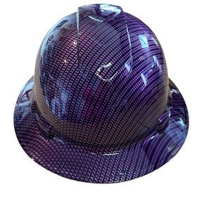 Könnte beinhalten: Lilafarbener Schutzhelm mit einem Karbonfaser-Muster. Der Helm hat einen breiten Rand und eine erhöhte Krone.