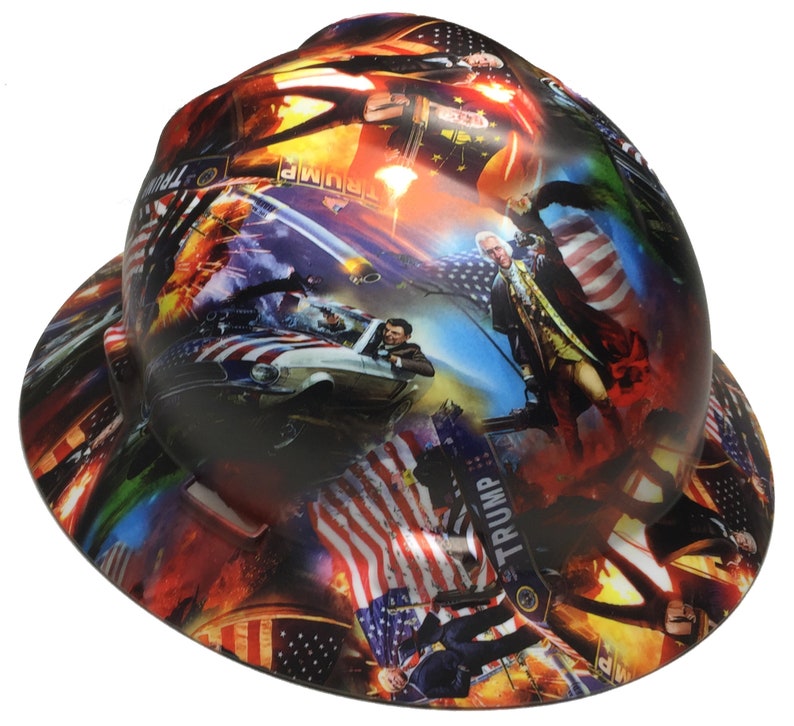 May include: A hard hat with a colorful graphic design featuring American flags, historical figures, and the word "TRUMP". The design includes images of a car, explosions, and a patriotic theme.