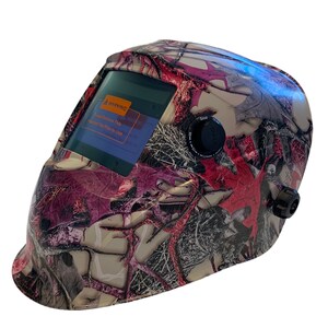 May include: A pink and grey camouflage welding helmet with a digital display and a warning label that reads "Please Remove This Welding Filter Prior to Use".