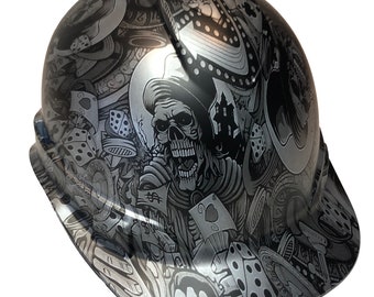 May include: A black hard hat with a silver skull and dice graphic design. The design includes playing cards, dollar signs, and other gambling imagery.