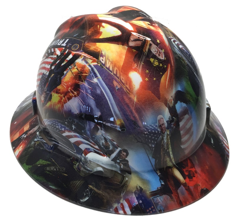 May include: A hard hat with a wrap-around graphic featuring patriotic imagery, including the American flag, historical figures, and a car chase scene. The hat has a glossy finish and a wide brim.