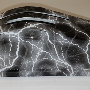 May include: A black and white lightning bolt patterned car part. The part is made of a hard plastic material and has a smooth, glossy finish.