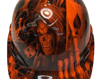 May include: Orange hard hat with a skull and flames graphic design. The design includes a playing card with a spade symbol.